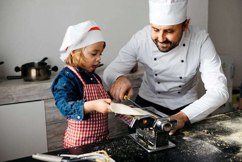 un chef aide une fille à faire des pâtes